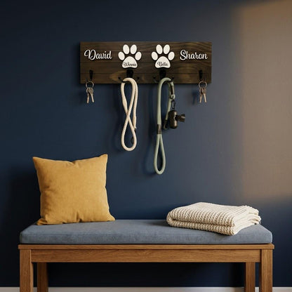 Personalized dog leash holder for wall with raised 3D names, engraved paw and black metal hooks on a stained pine board