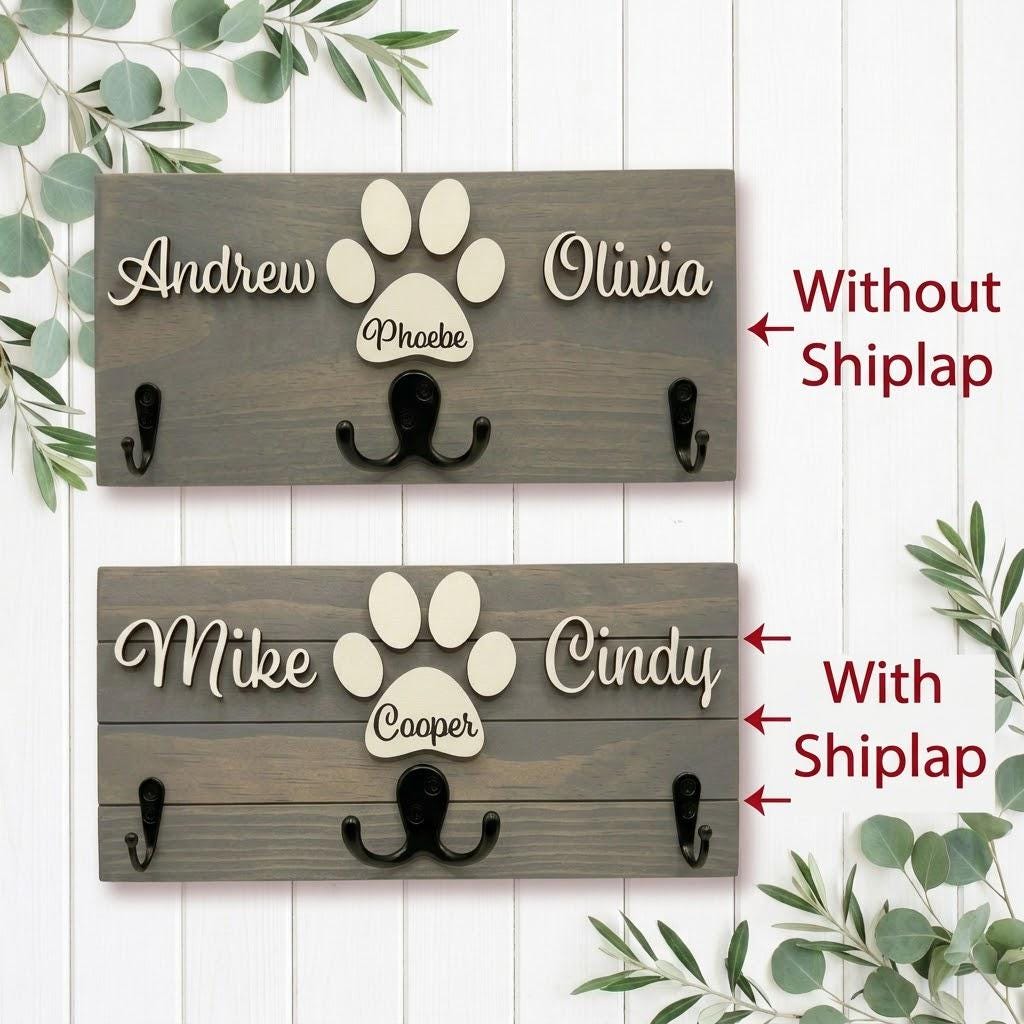 Personalized dog leash holder for wall with raised 3D names, engraved paw and black metal hooks on a stained pine board